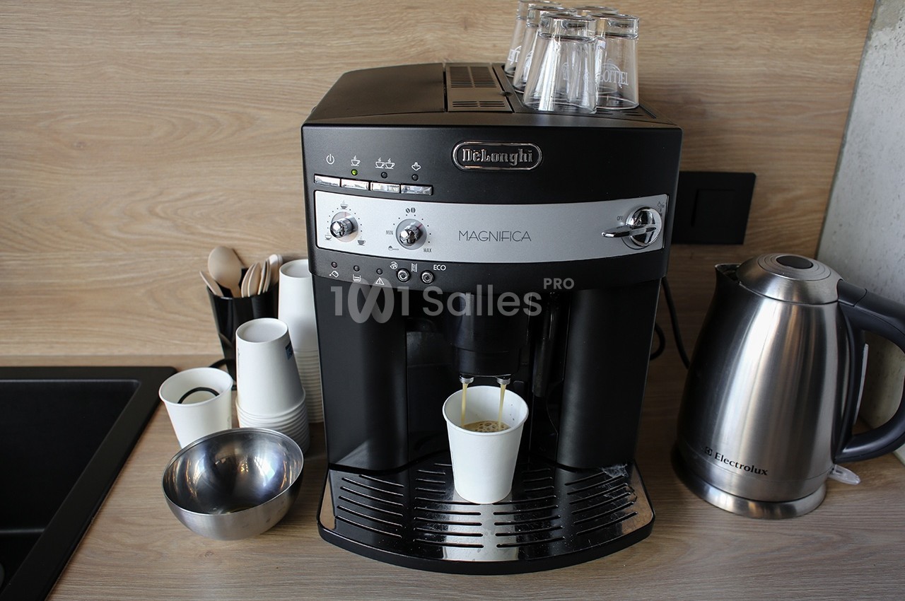 Machine à café automatique avec gobelet en cours de remplissage, posée sur un plan de travail avec accessoires à proximité.