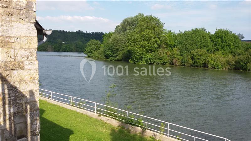 Vue d'une rivière bordée de végétation dense, avec un mur en pierre et une balustrade au premier plan.
