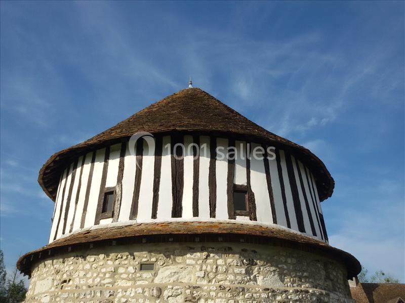 Bâtiment circulaire à colombages et toit en chaume, sur une base en pierre, sous un ciel bleu dégagé.