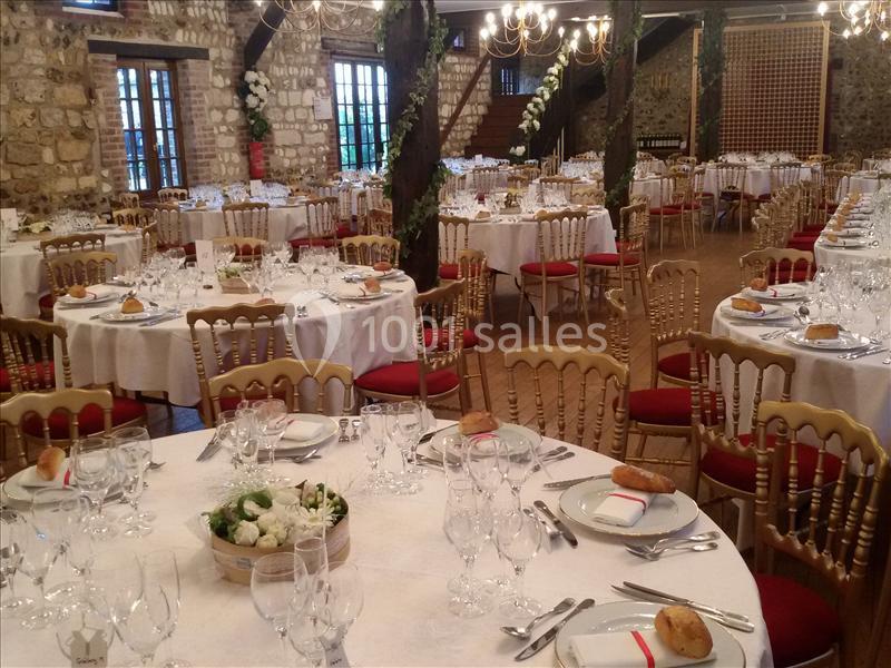 Salle de réception décorée avec des tables rondes dressées, nappes blanches, chaises dorées et éclairage chaleureux.
