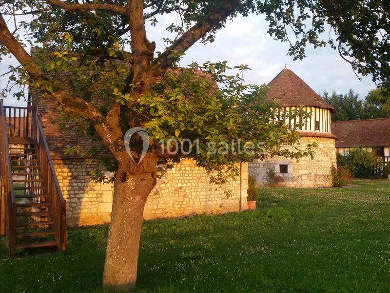 Arbre devant un bâtiment en pierre avec toit en tuiles, éclairé par une lumière douce en fin de journée.