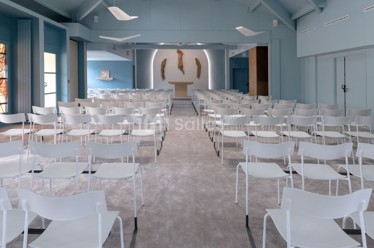 Salle de cérémonie moderne avec des chaises blanches alignées face à un autel et des sculptures murales.