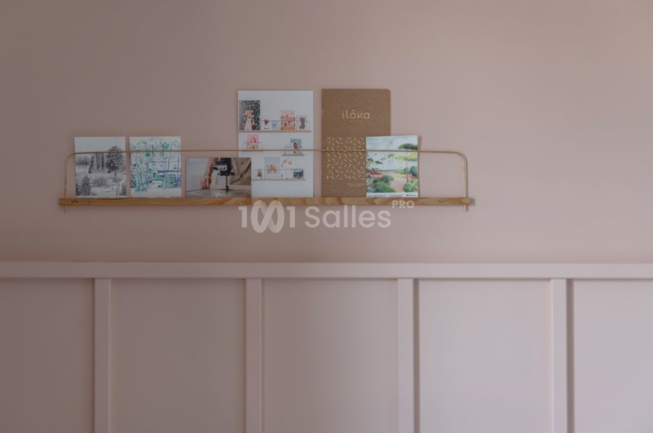Étagère murale en bois clair avec des cartes illustrées et un carnet beige, sur un mur rose pastel.