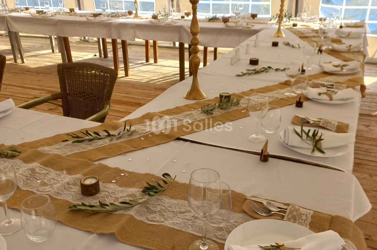 Tables décorées pour un événement avec nappes blanches, chemins de table en toile de jute, fleurs et vaisselle.