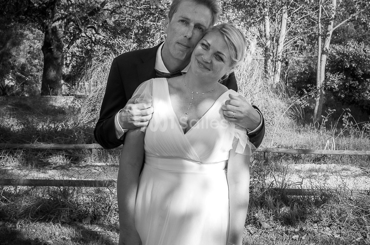 Un couple en tenue de mariage pose tendrement dans un cadre naturel avec des arbres en arrière-plan.