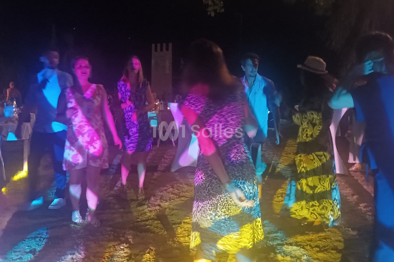 Des personnes dansent en groupe en extérieur, éclairées par des lumières colorées, dans une ambiance festive nocturne.