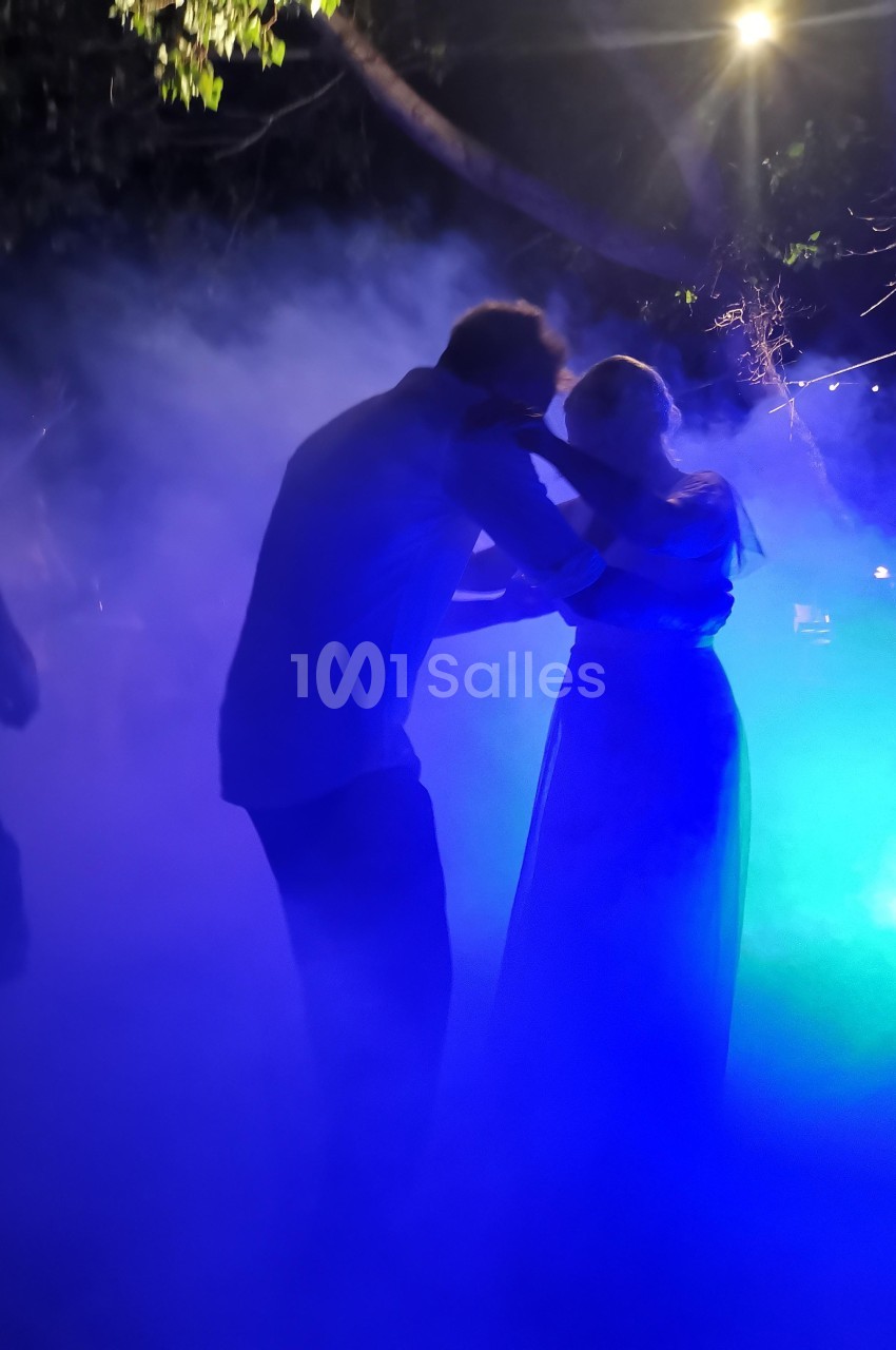 Un couple danse dans une ambiance nocturne éclairée par des lumières colorées et entourée de fumée.