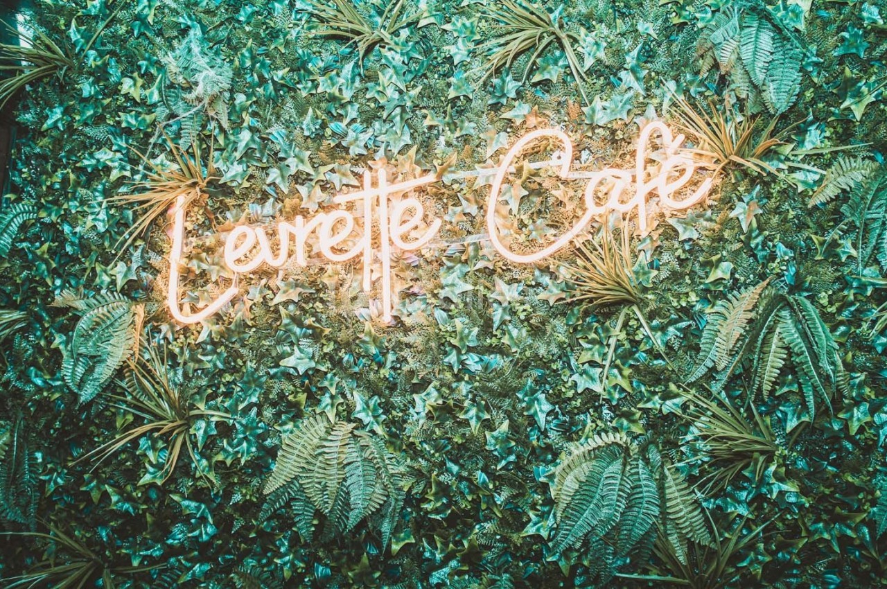 Mur végétal avec une enseigne lumineuse néon indiquant ’Levrette Café’ au centre.