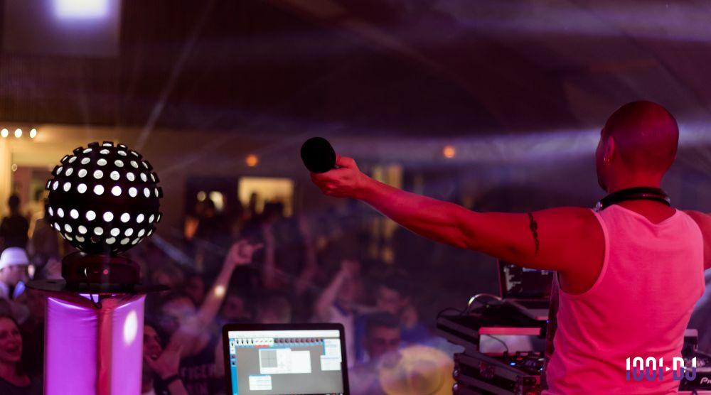 Un DJ anime une soirée festive avec une foule dansante, des jeux de lumière et du matériel audio visible.