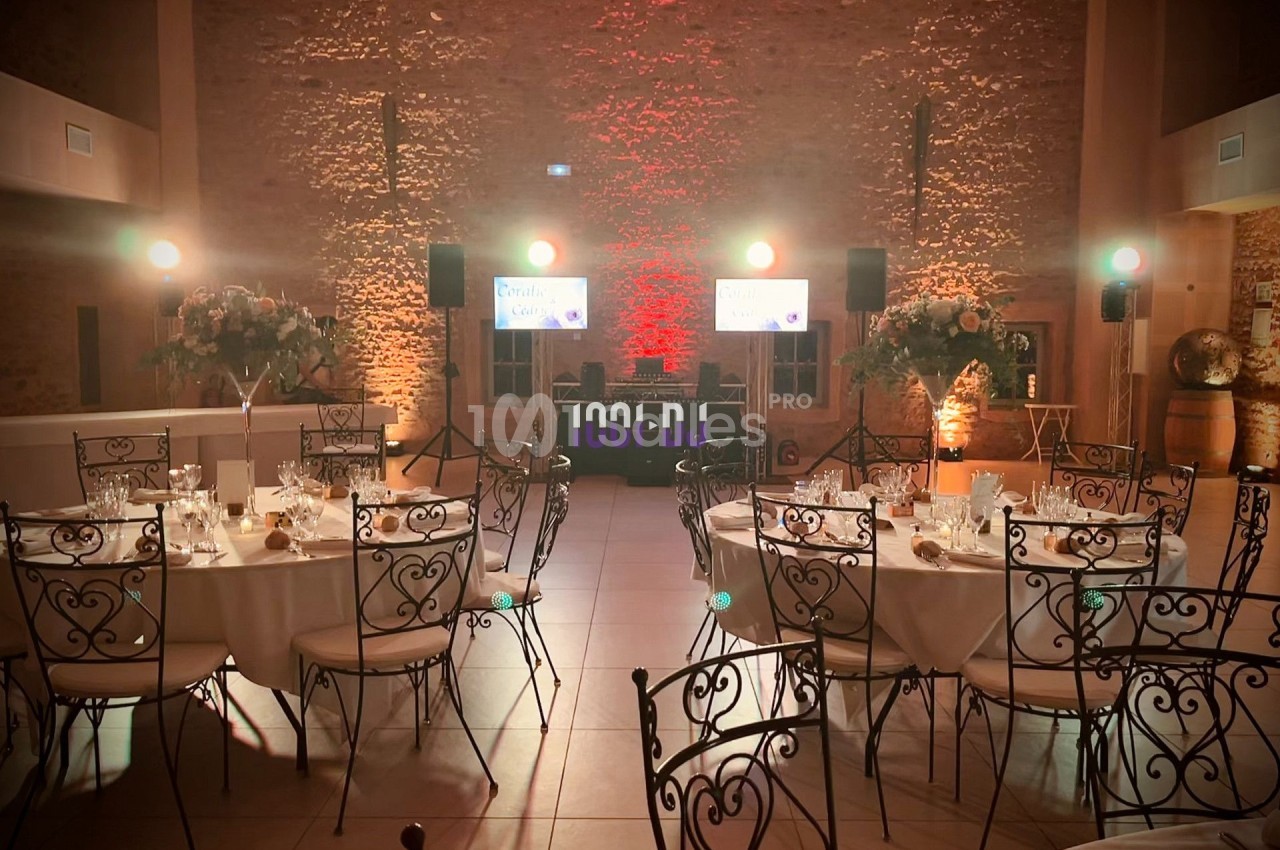Salle de réception décorée avec des tables rondes dressées, chaises en fer forgé et éclairage chaleureux.
