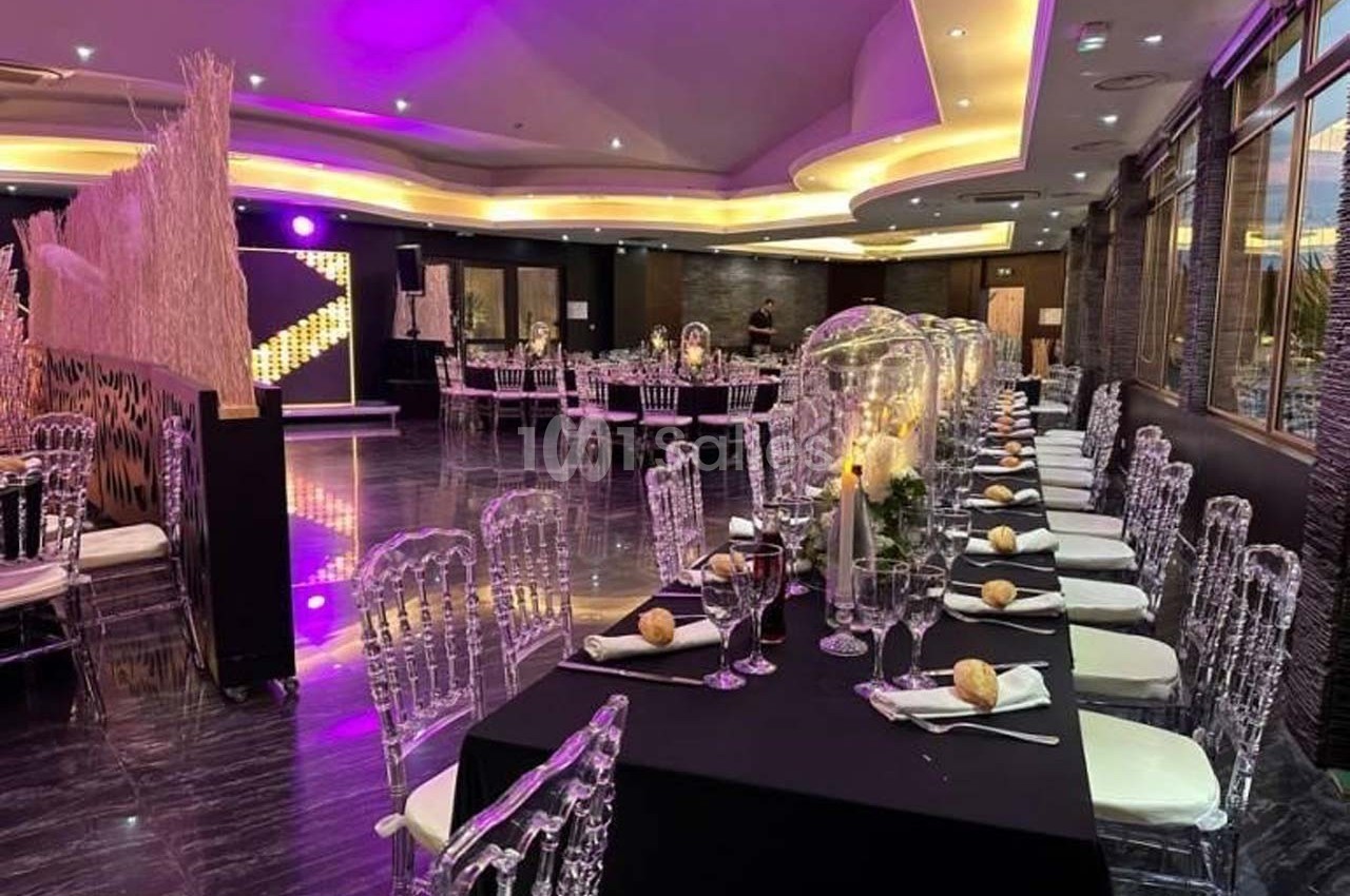 Salle de réception élégante avec tables dressées, chaises transparentes et éclairage d'ambiance violet.
