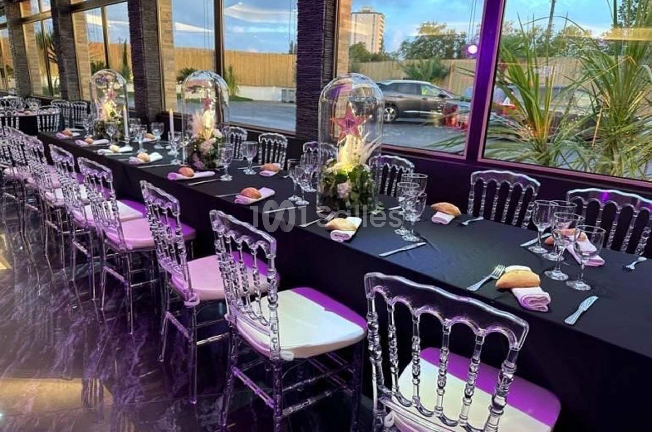 Salle de réception avec longues tables noires décorées de centres de table floraux et chaises transparentes.