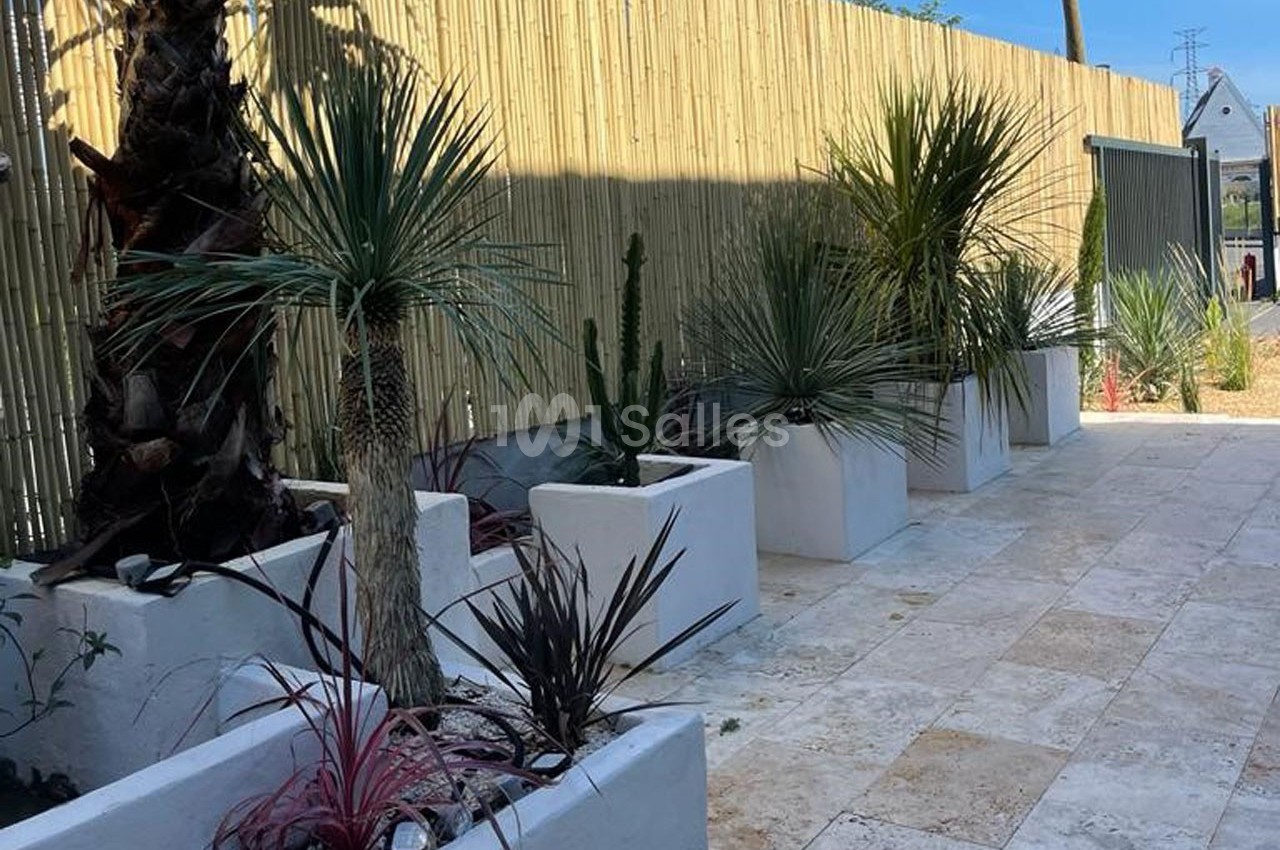 Plantes méditerranéennes en pots blancs alignées le long d'une clôture en bambou sur une terrasse en pierre.