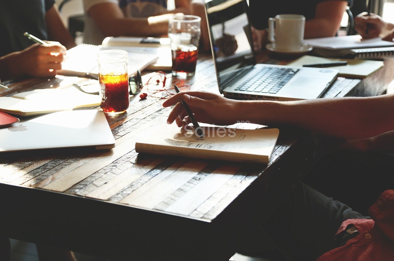 Personnes travaillant autour d'une table en bois avec ordinateurs, carnets et boissons.