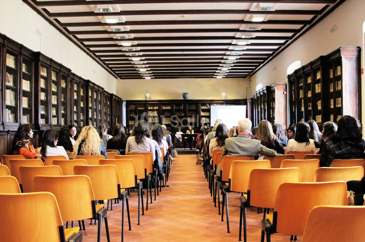 Salle de conférence avec des rangées de chaises orange, des participants assis et un écran de présentation au fond.