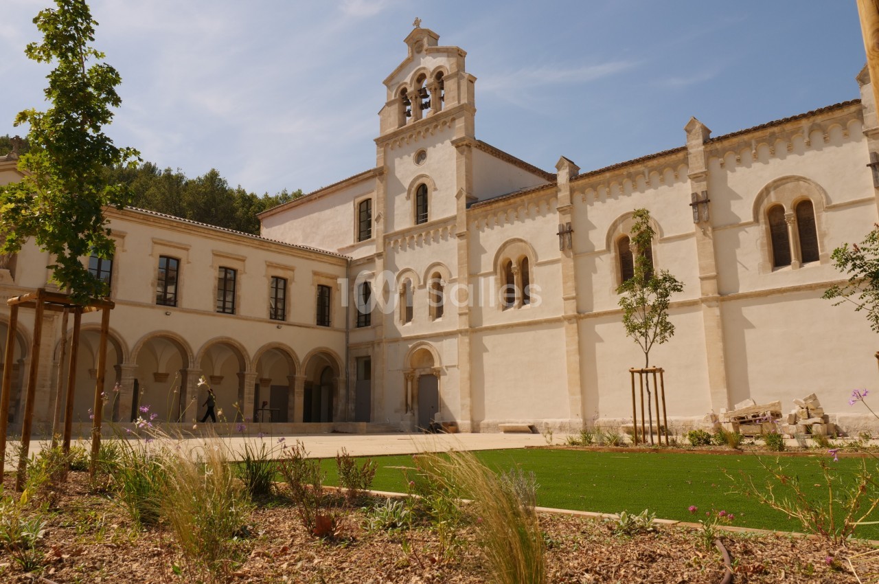 Façade d'un bâtiment historique en pierre blanche avec clocher, entouré d'un jardin paysager sous un ciel dégagé.