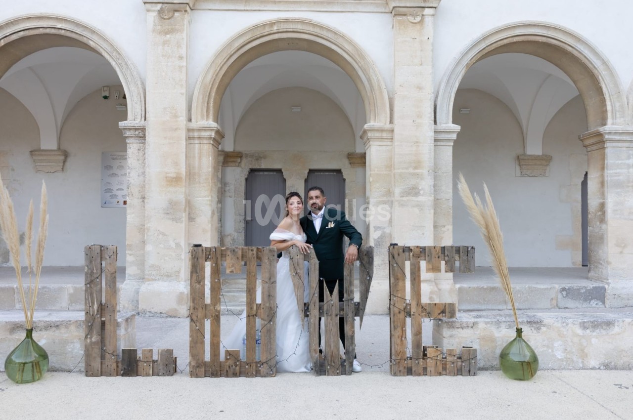 Un couple en tenue de mariage pose devant des arches en pierre et des lettres formant le mot ’LOVE’.