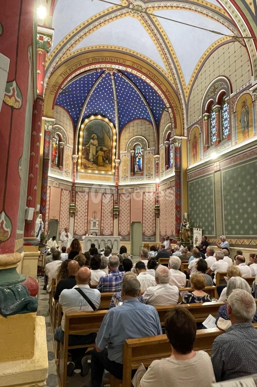 Intérieur d'une église avec des fidèles assis, ornée de fresques colorées, vitraux et voûtes décorées.