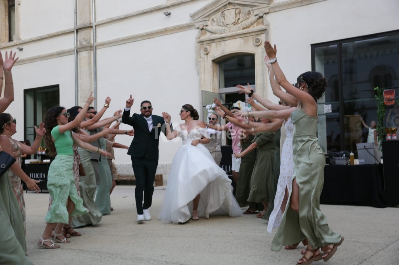 Un couple de mariés danse entouré d'invités en tenue festive dans une cour extérieure.