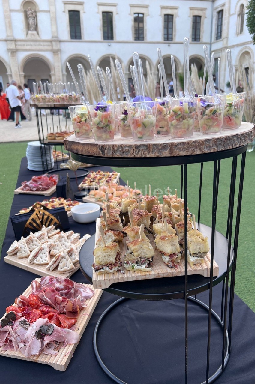 Buffet en plein air avec verrines, sandwichs et charcuterie, installé dans une cour avec bâtiment historique en arrière-plan.
