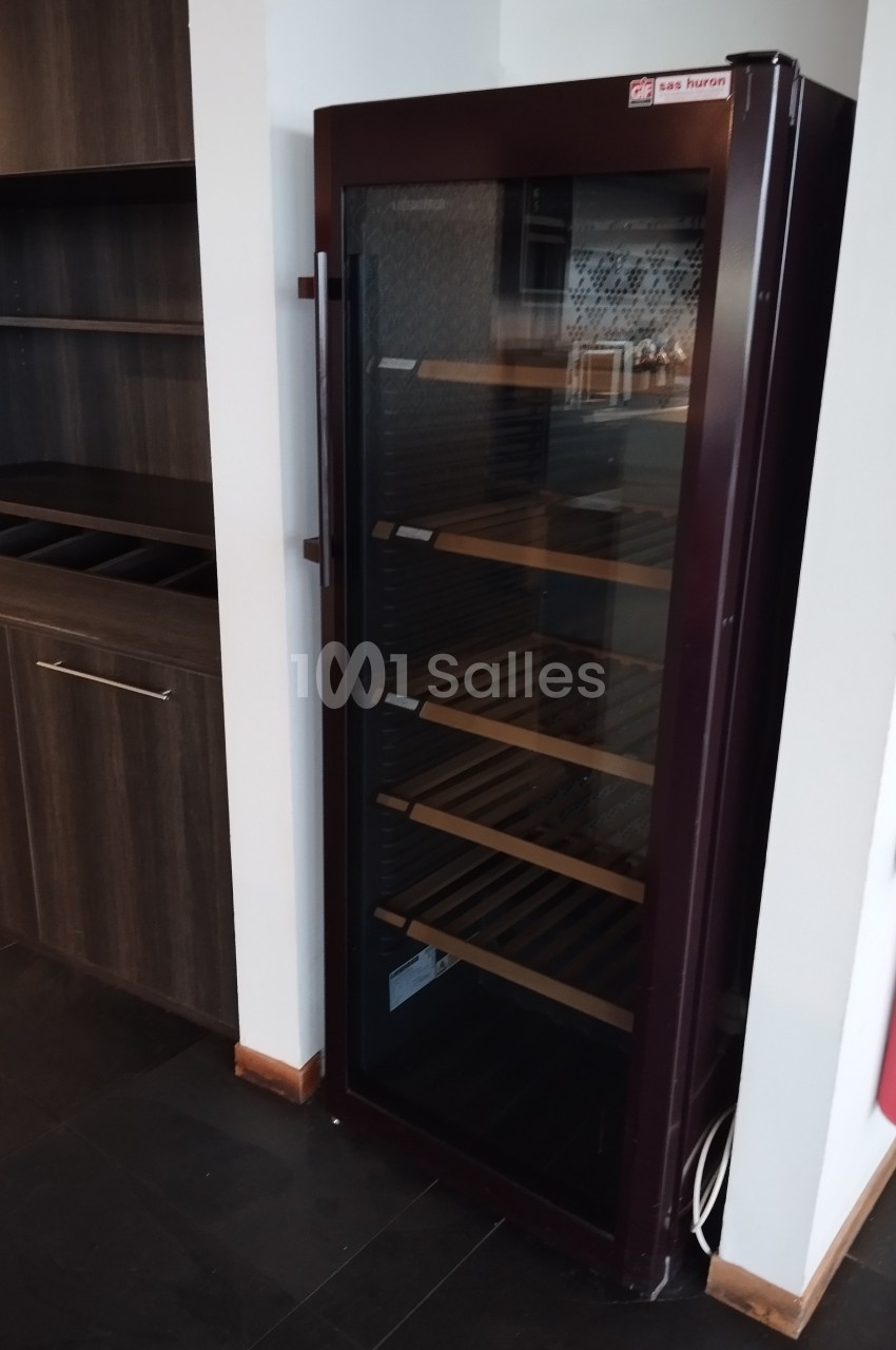 Armoire à vin vitrée avec étagères en bois, placée dans un coin d'une pièce avec des meubles en bois sombre.