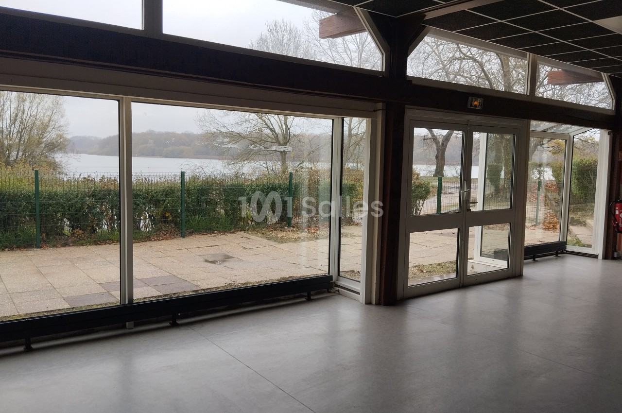 Vue intérieure d'une salle avec de grandes baies vitrées donnant sur un paysage extérieur arboré et un plan d'eau.