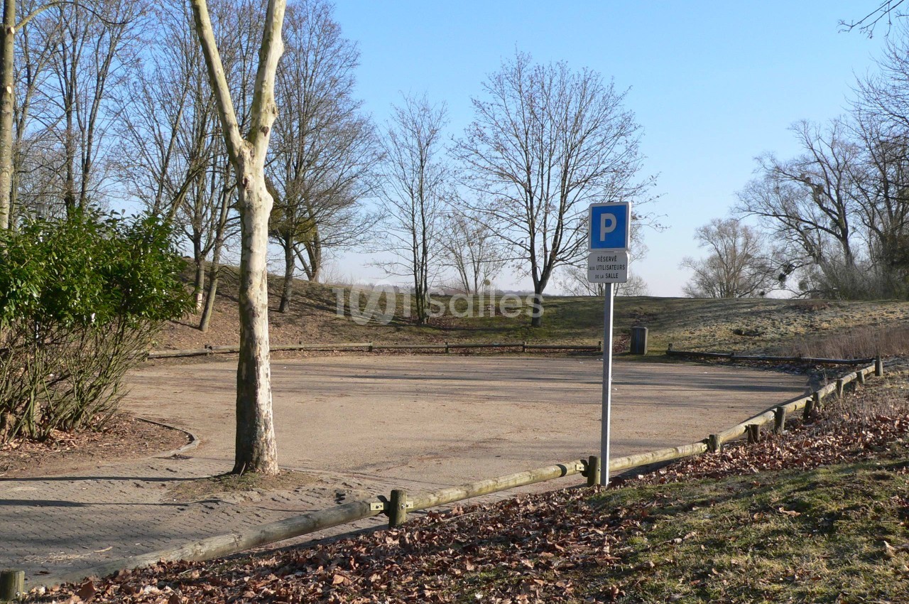 Parking vide en plein air entouré d'arbres en hiver, avec un panneau indiquant une zone de stationnement.