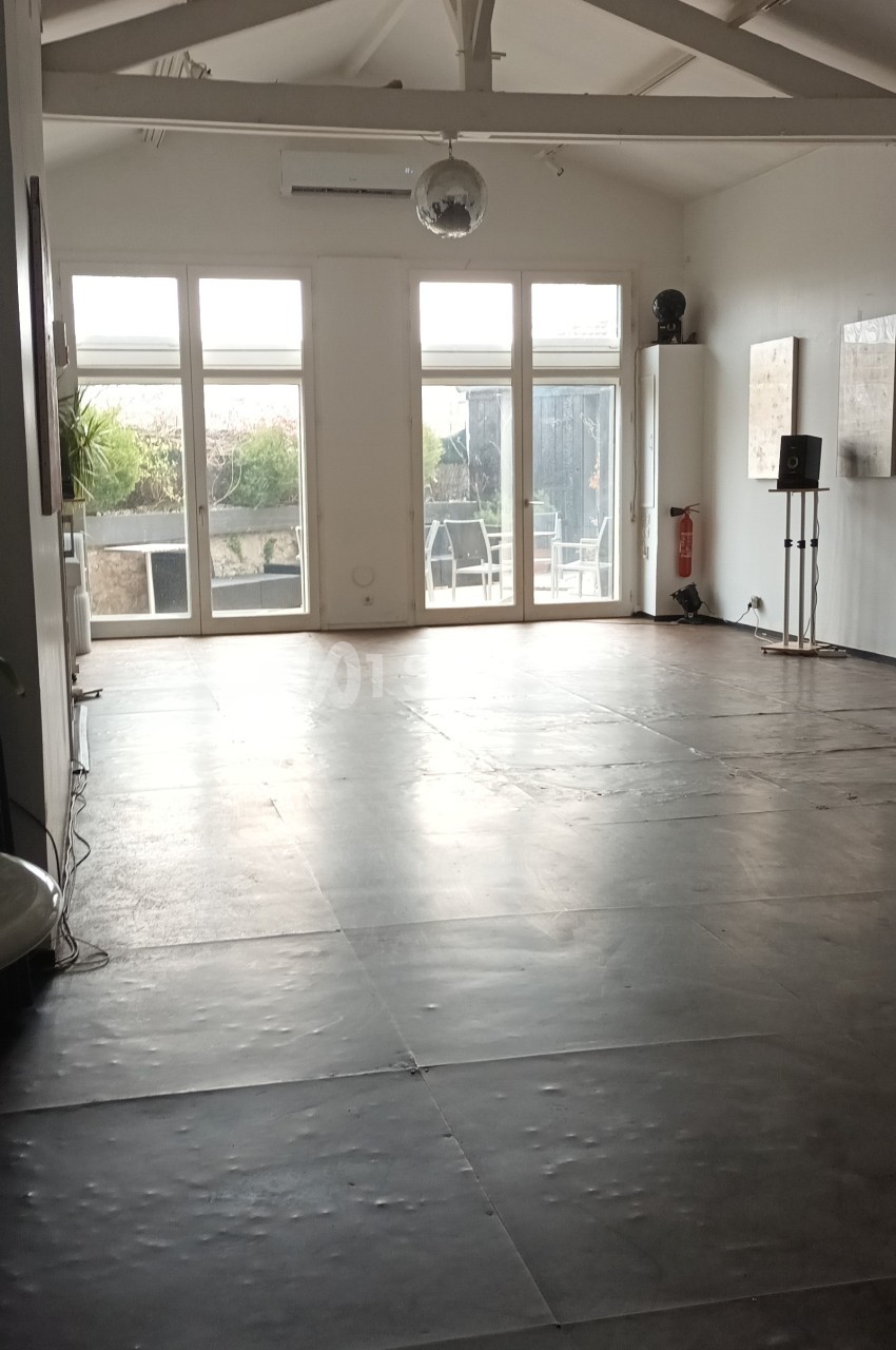Salle lumineuse avec un sol en béton, des murs blancs, une grande baie vitrée et une boule disco suspendue.