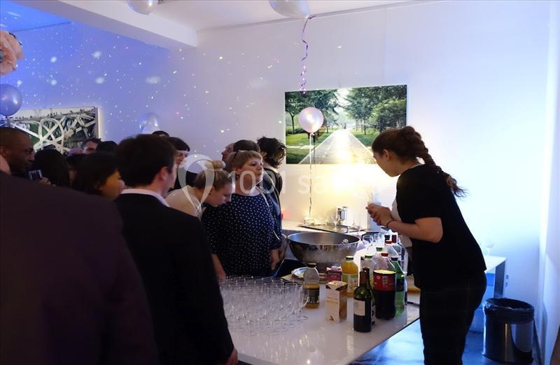 Un groupe de personnes rassemblées autour d'un bar lors d'un événement dans une salle décorée de ballons et lumières.