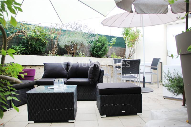 Salon de jardin en résine tressée noire avec table basse et parasols sur une terrasse carrelée entourée de végétation.