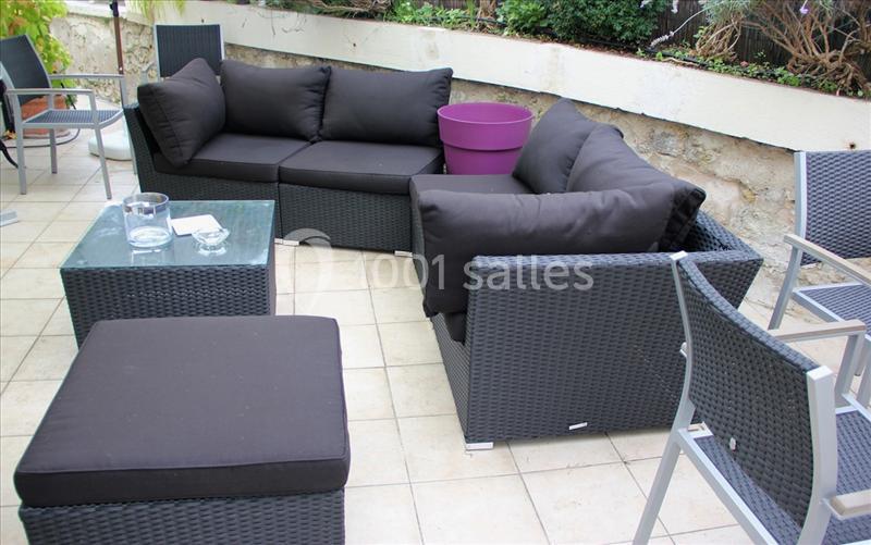 Salon de jardin en résine tressée noire avec coussins noirs, table basse en verre et pot violet sur une terrasse carrelée.