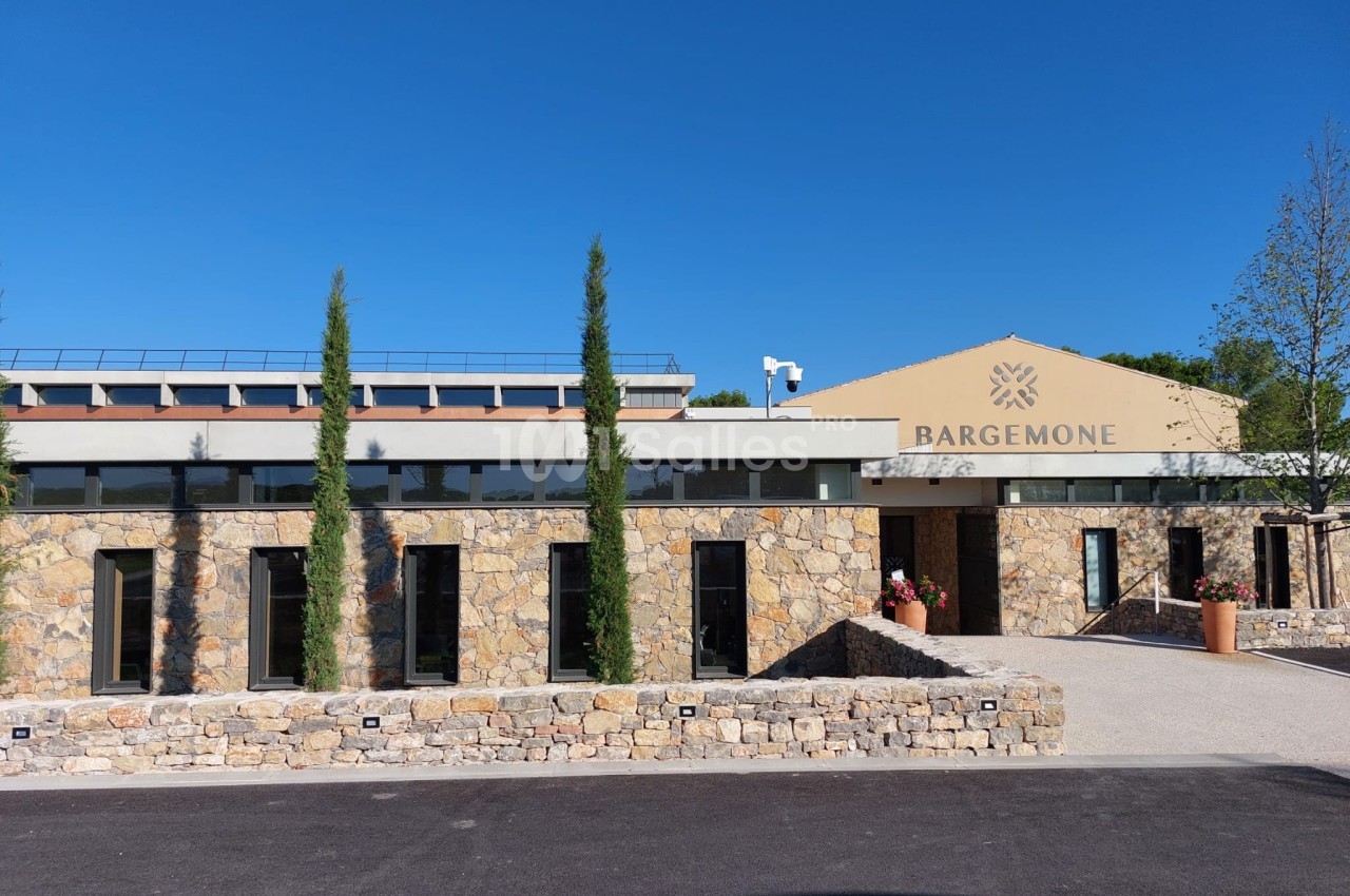 Bâtiment en pierre avec façade moderne, arbres élancés et enseigne ’Bargemone’ sous un ciel bleu clair.