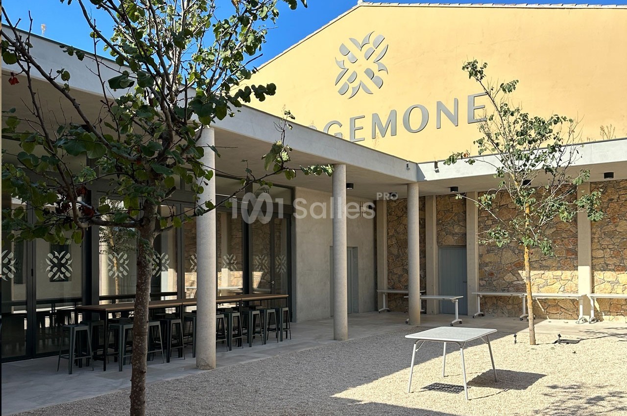 Cour extérieure avec tables, arbres et façade d’un bâtiment beige portant l’inscription ’CEMONE’.