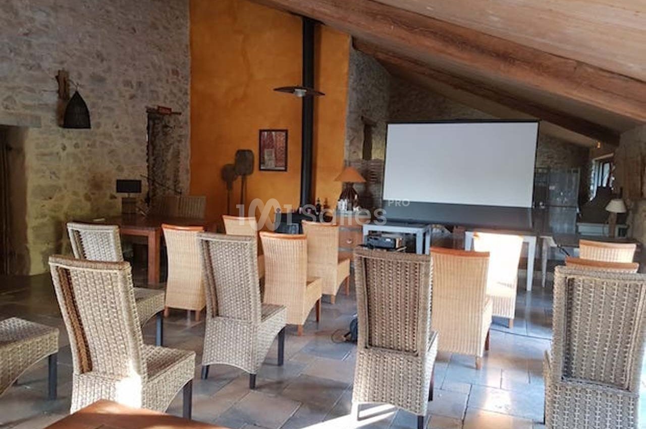 Salle de réunion avec des chaises en osier disposées face à un écran de projection dans un espace en pierre et bois.