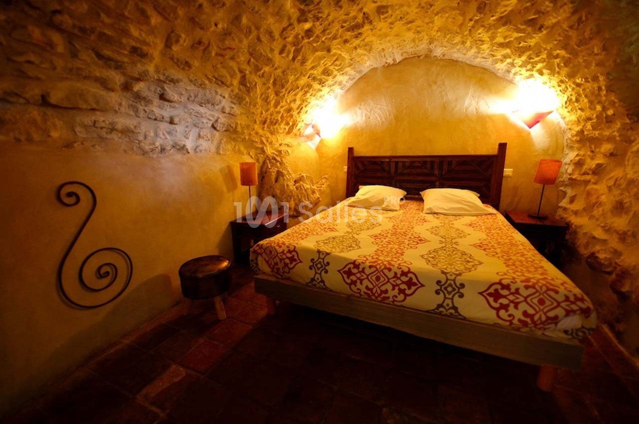 Chambre rustique avec murs en pierre, lit double, éclairage tamisé et décoration chaleureuse.