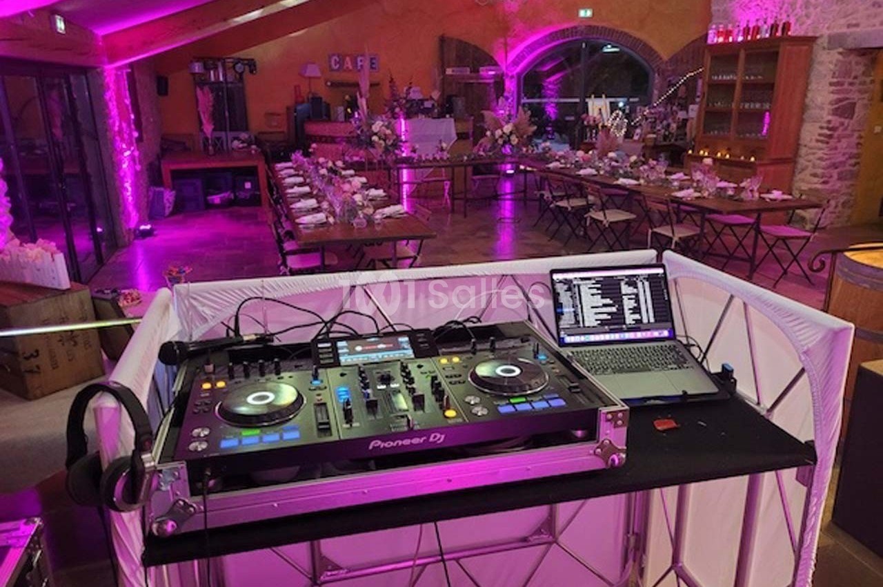 Poste de DJ avec platines et ordinateur portable dans une salle de réception décorée pour un événement festif.