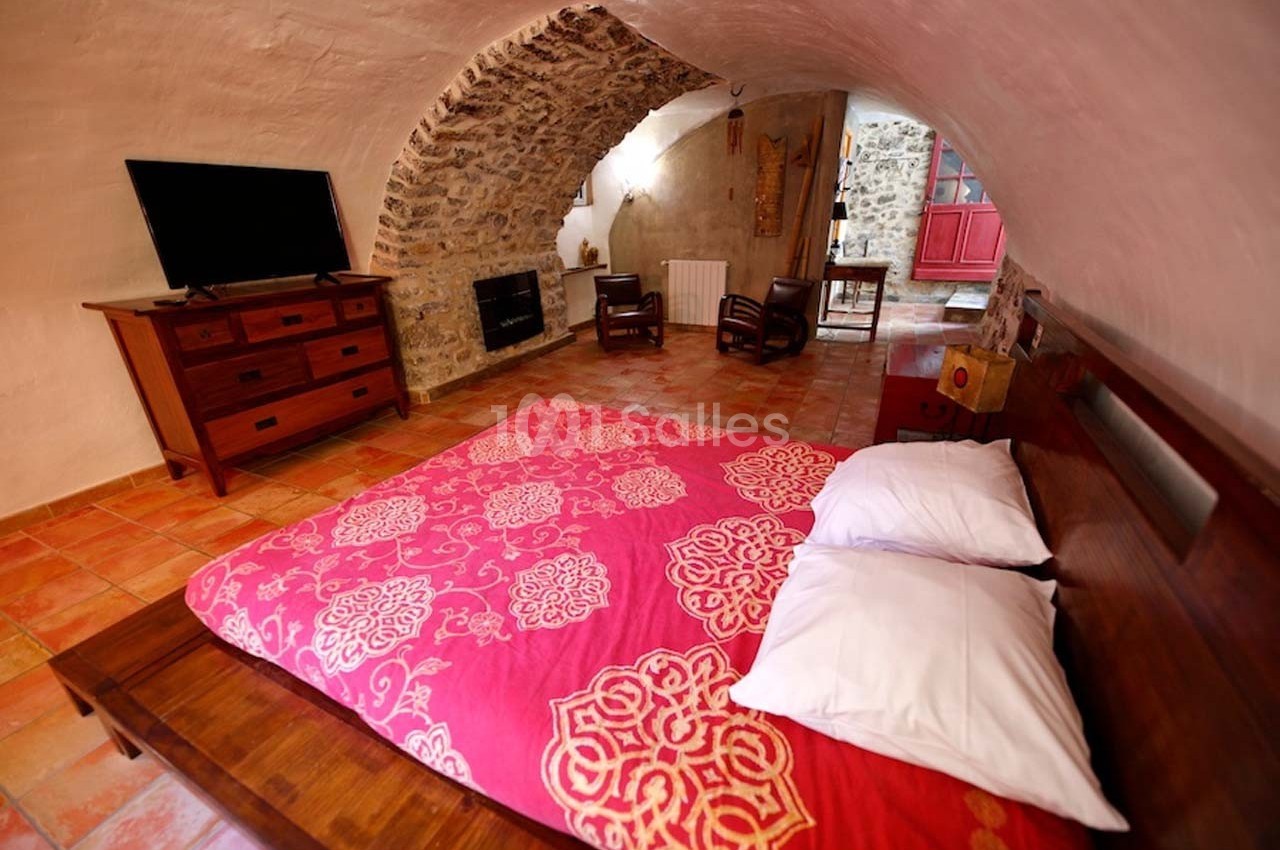 Chambre voûtée avec lit double, couvre-lit rouge à motifs, mobilier en bois, téléviseur et sol en carrelage.