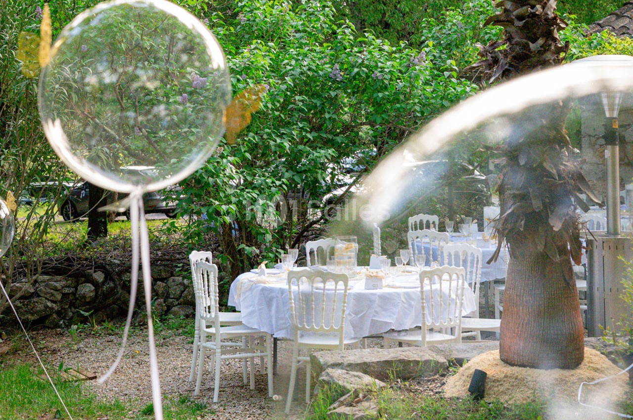 Tables dressées avec nappes blanches dans un jardin verdoyant, entourées de chaises blanches et de végétation.