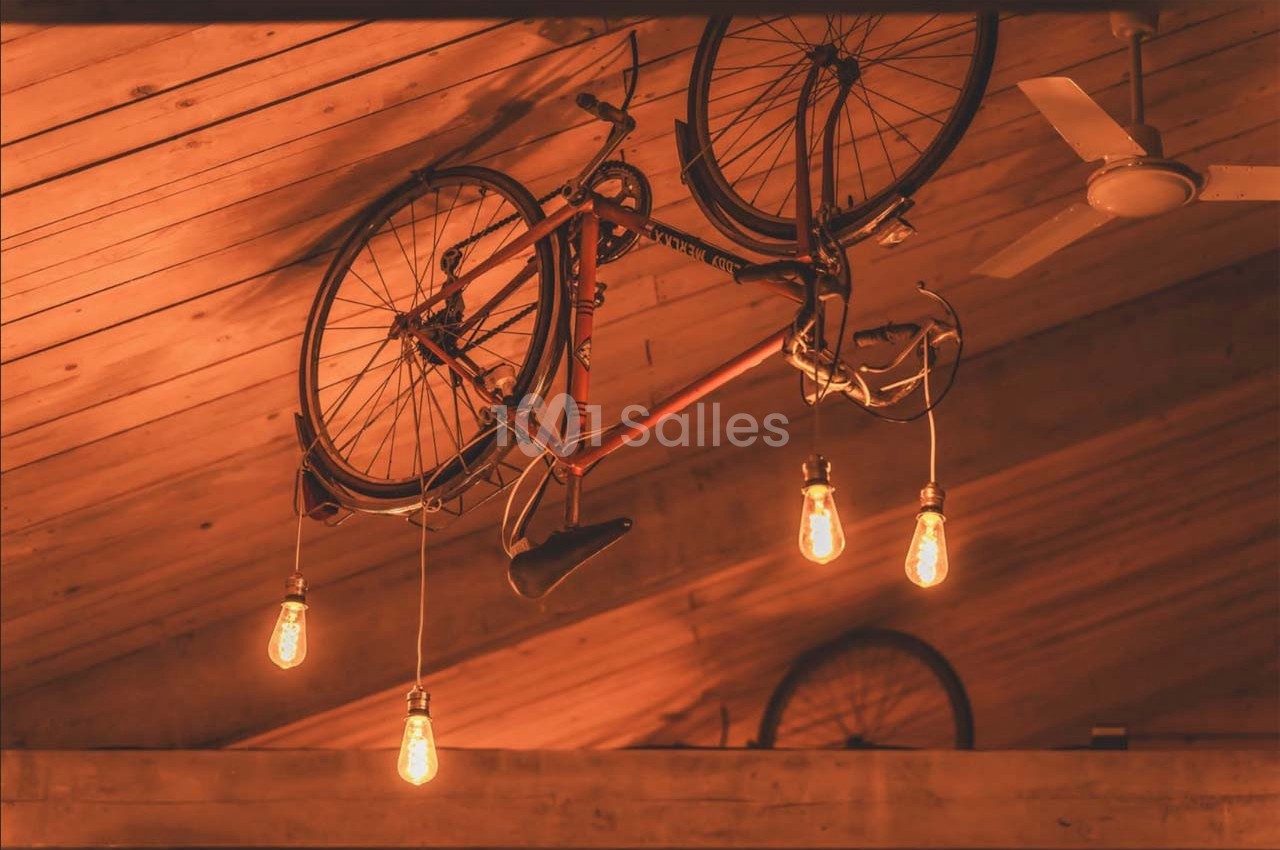 Un vélo suspendu au plafond en bois, entouré d'ampoules suspendues diffusant une lumière chaude.
