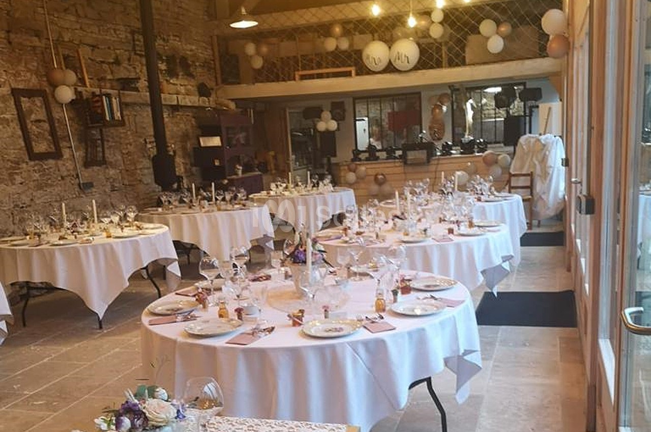 Salle de réception décorée avec des tables rondes dressées, ornées de fleurs et de ballons suspendus.