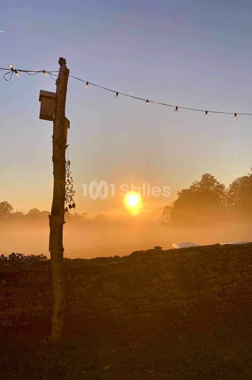 Lever de soleil sur un paysage brumeux avec un mur de pierre, un poteau en bois et une guirlande lumineuse.
