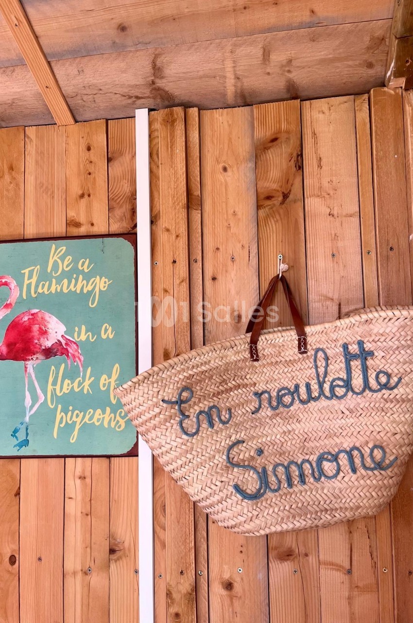 Panneau avec un flamant rose et un panier en osier suspendu, inscrit ’En route Simone’, sur un mur en bois.