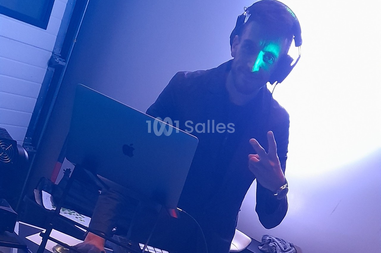 Un DJ mixant sur un ordinateur portable dans une ambiance lumineuse bleutée.