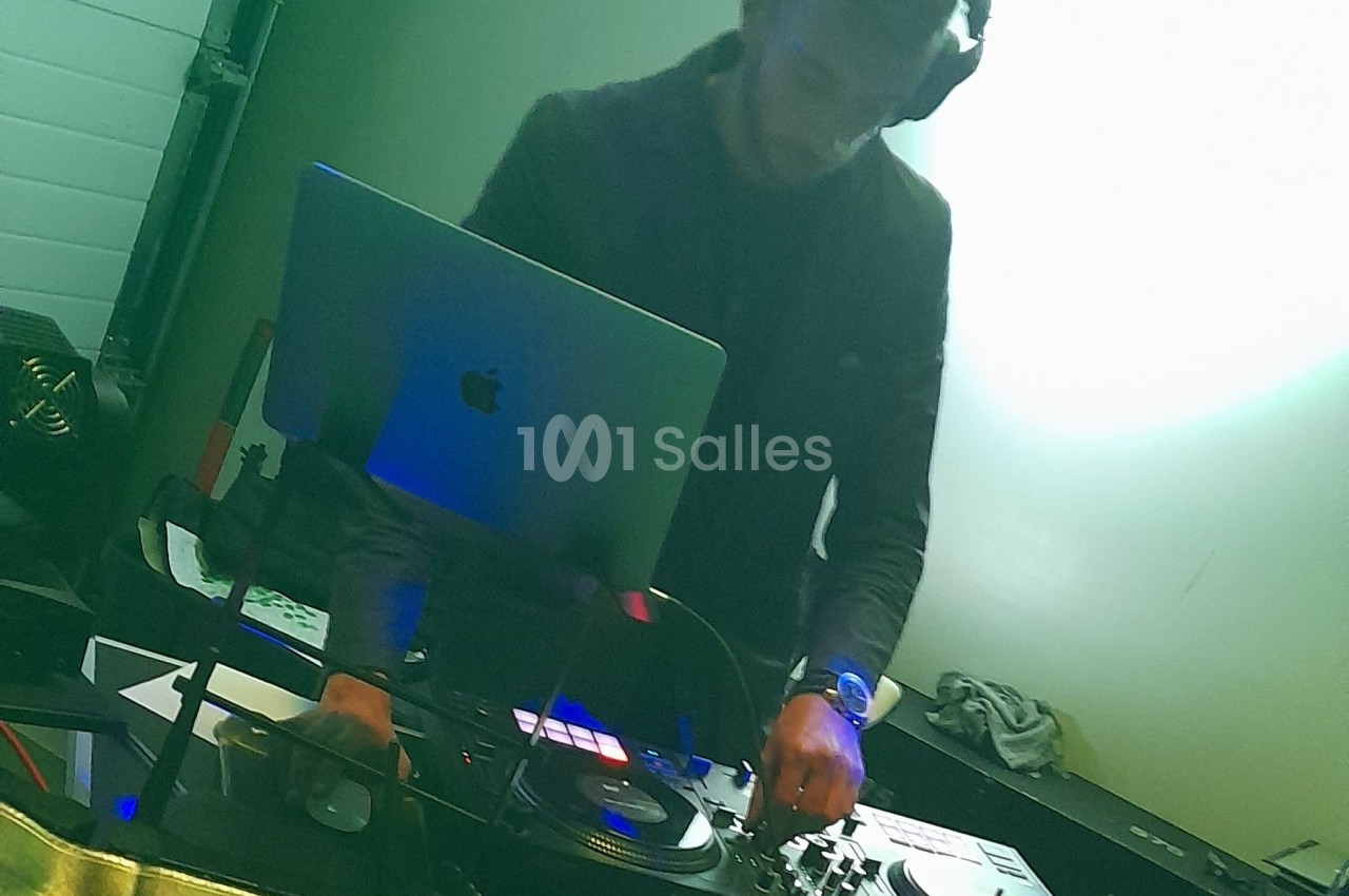 Un DJ mixant de la musique sur une table de mixage avec un ordinateur portable dans un environnement lumineux.