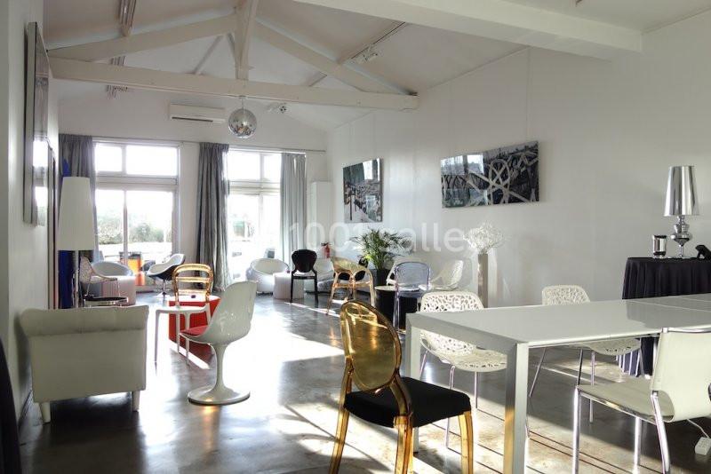 Salle lumineuse avec mobilier moderne, grandes fenêtres, plafond avec poutres apparentes et décoration contemporaine.