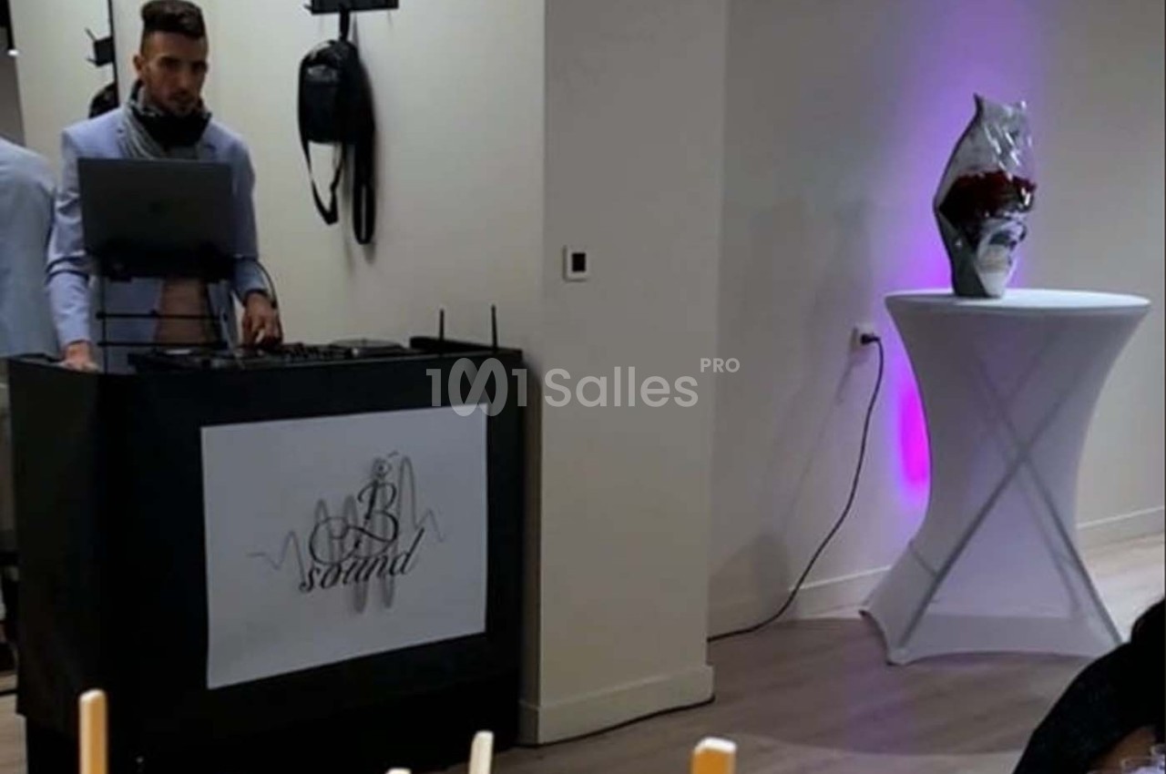 Un DJ mixe derrière une table de sonorisation dans une salle éclairée, avec une table haute décorative à côté.