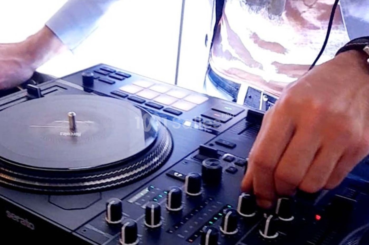 Un DJ ajuste les commandes d'une table de mixage avec une platine vinyle en arrière-plan.