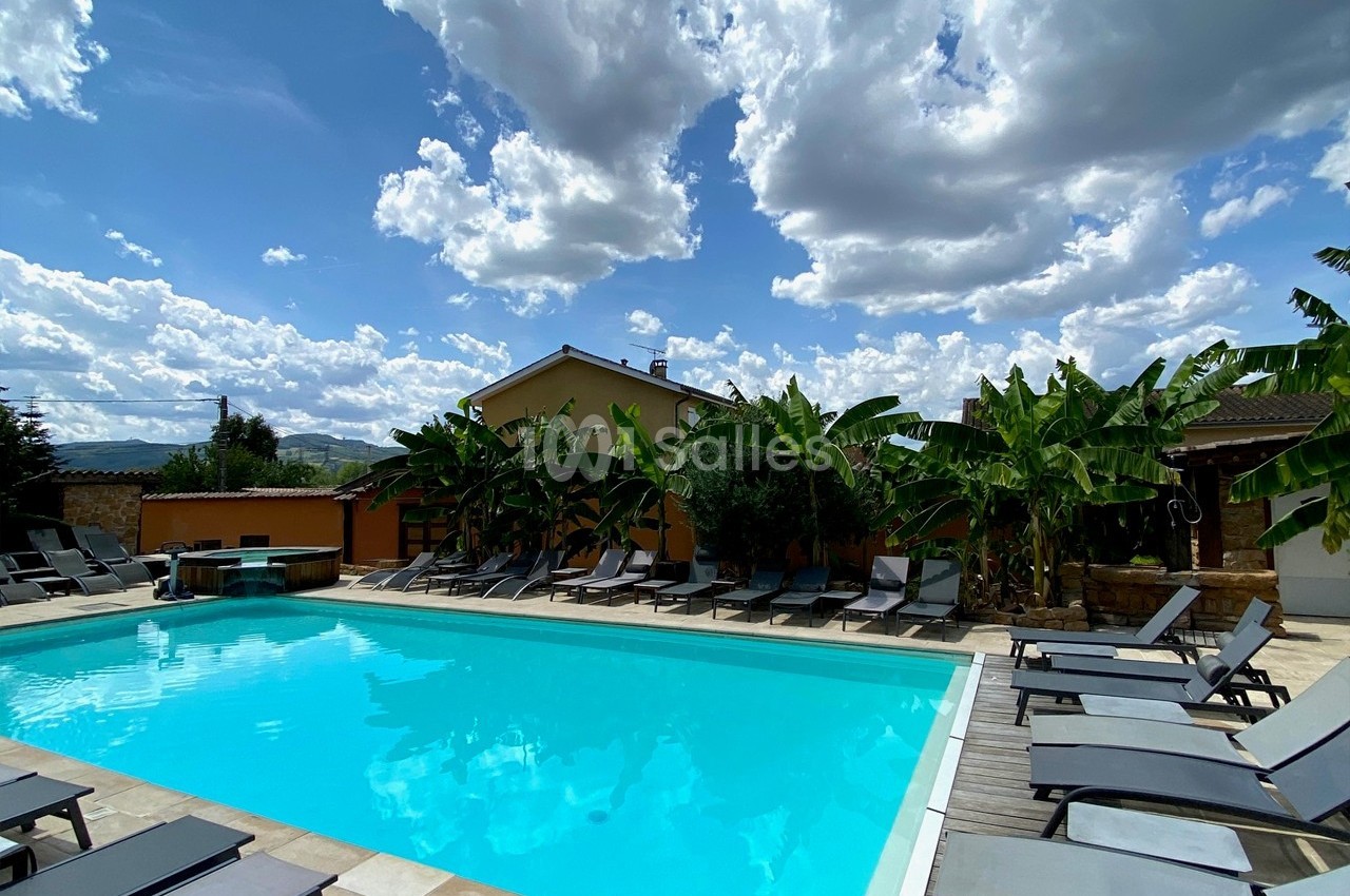 Piscine extérieure entourée de transats, de bananiers et d'un ciel partiellement nuageux.