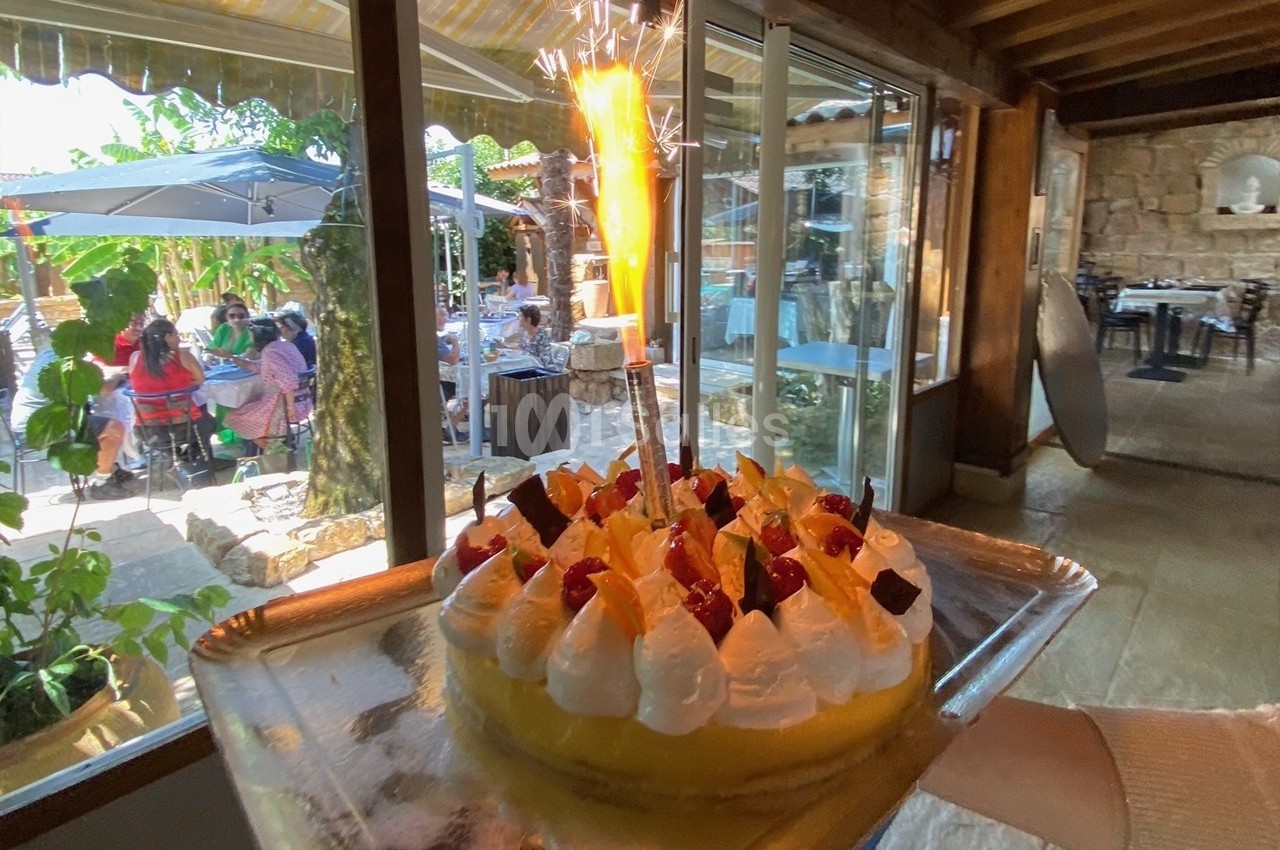 Gâteau décoré de fruits et de crème avec une bougie étincelante, présenté dans un restaurant lumineux.