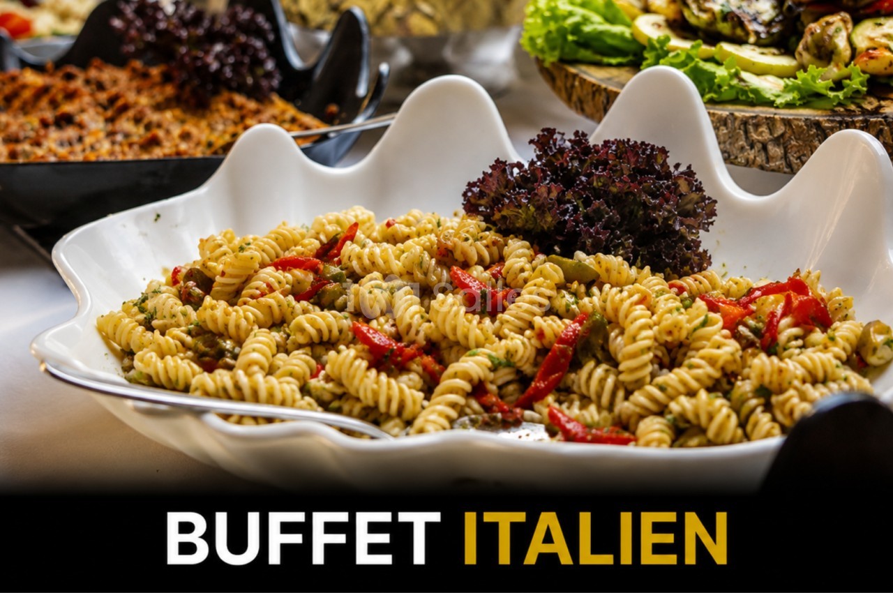 Assiette de pâtes fusilli garnies de légumes et herbes, présentée sur un buffet avec d'autres plats variés.
